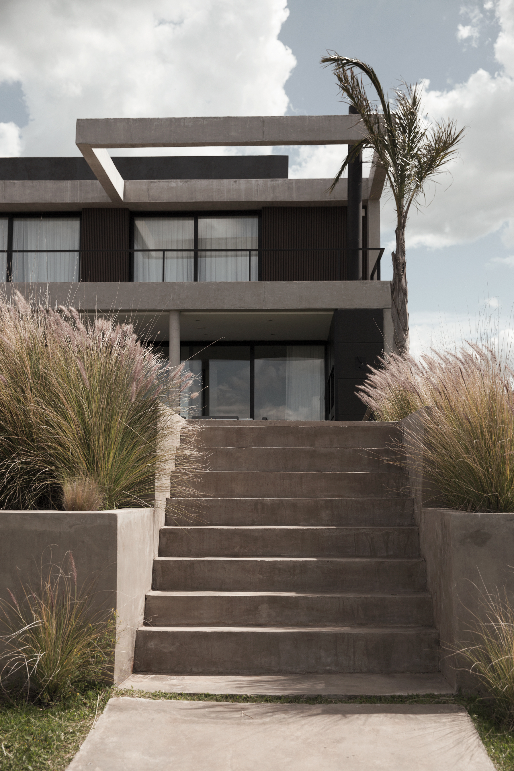 Fachada frontal con escalera de hormigón y paisajismo proyecto Costas